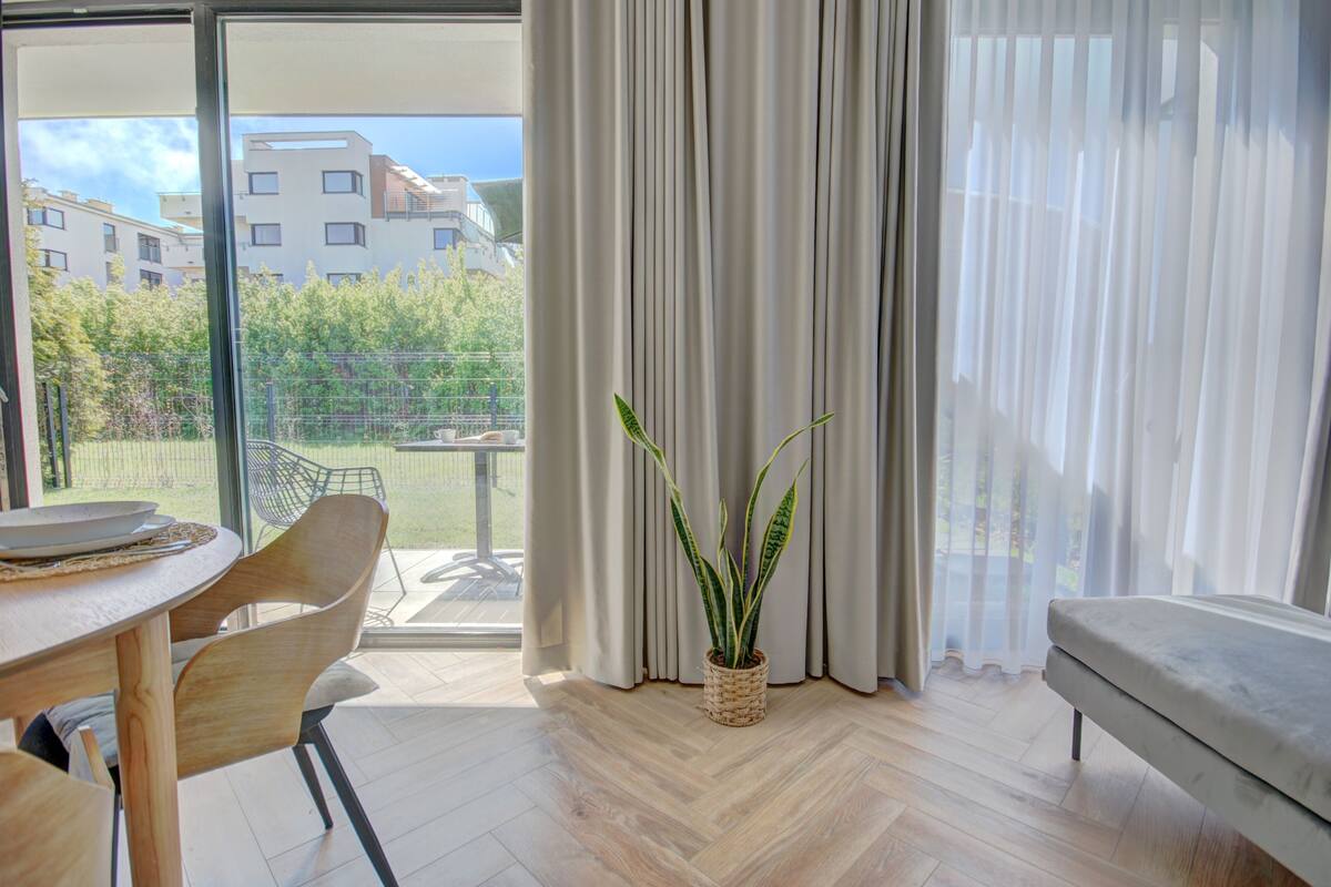 A modern living room with a wooden dining table, chairs, a sofa, and a potted plant.