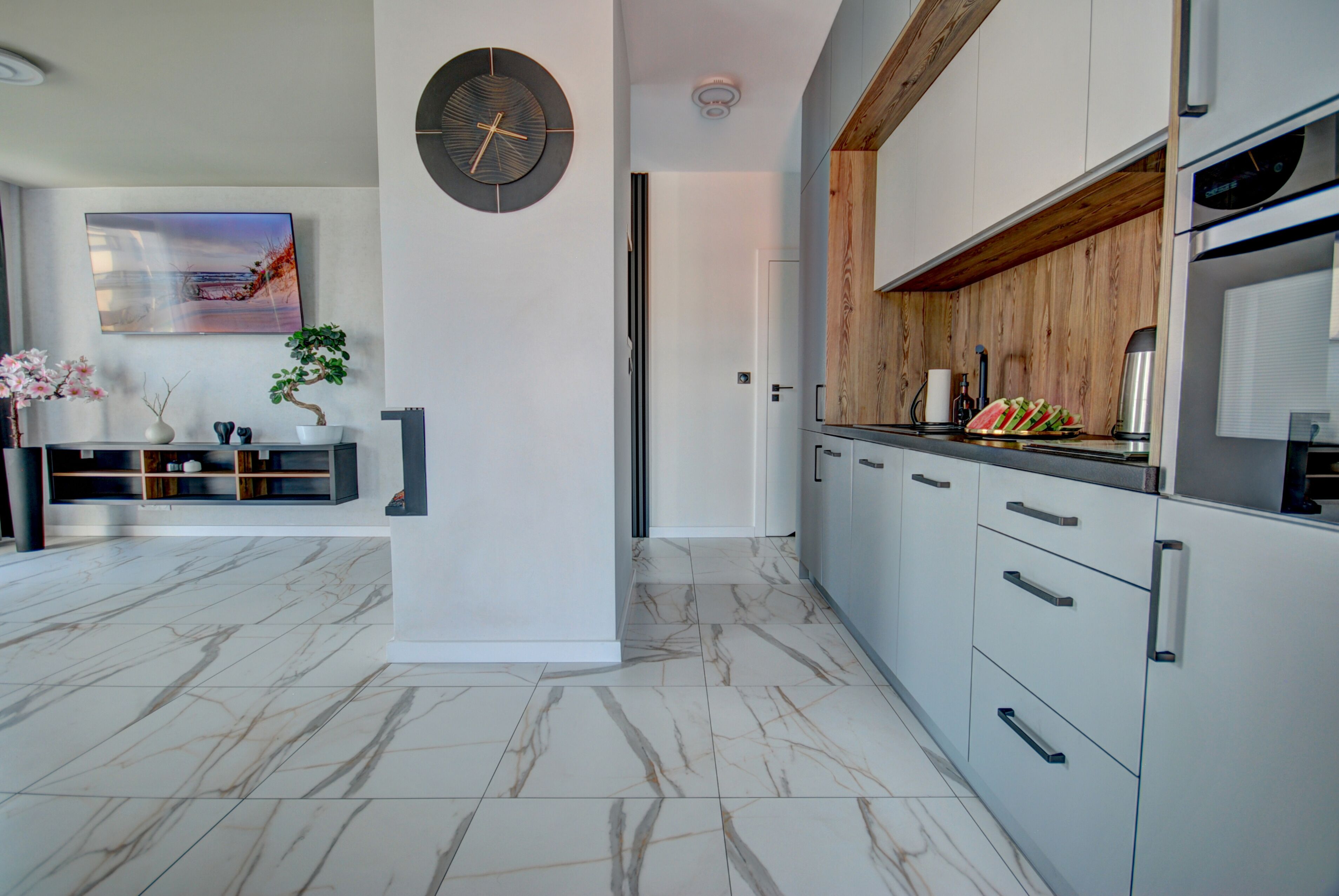 Une cuisine moderne avec un sol en marbre, des meubles en bois et une grande horloge au mur.