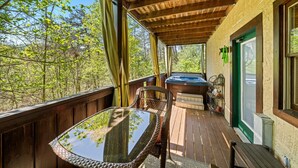 A wooden deck with a glass-top table and chairs, a hot tub, and a door with a green frame. - Smoky Mountain Getaway: Leave the World Behind (Pigeon Forge)