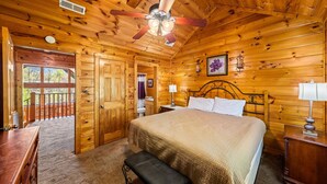 A wooden cabin bedroom with a bed, bench, ceiling fan, and a view through an open door. - Smoky Mountain Getaway: Leave the World Behind (Pigeon Forge)