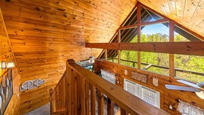 A wooden cabin interior with a high ceiling, wooden beams, and a large window offering a view of greenery. - Smoky Mountain Getaway: Leave the World Behind (Pigeon Forge)