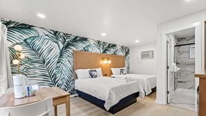 Ein Schlafzimmer mit zwei Betten, einem hölzernen Kopfteil, einem Nachttisch mit Lampe und einer Wand mit großem tropischen Blattmuster.