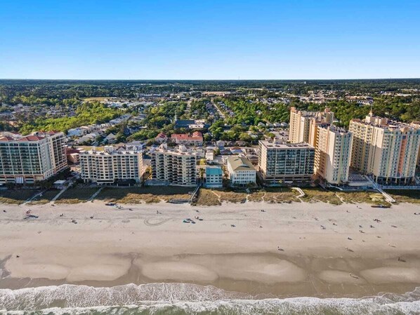 A coastal cityscape with high-rise buildings, a sandy beach, and a clear blue sky.