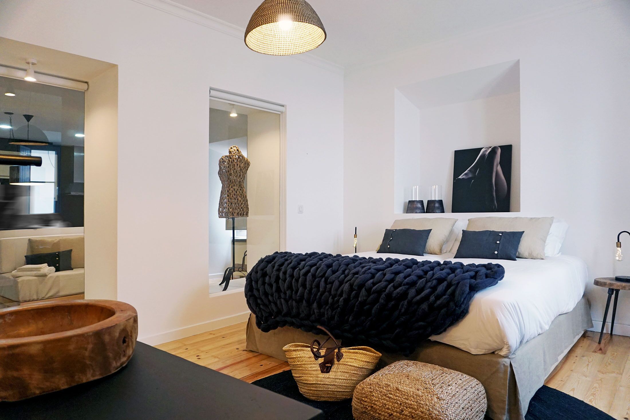 A modern bedroom with a large bed, a mirror, a wooden bowl, and a black throw blanket.