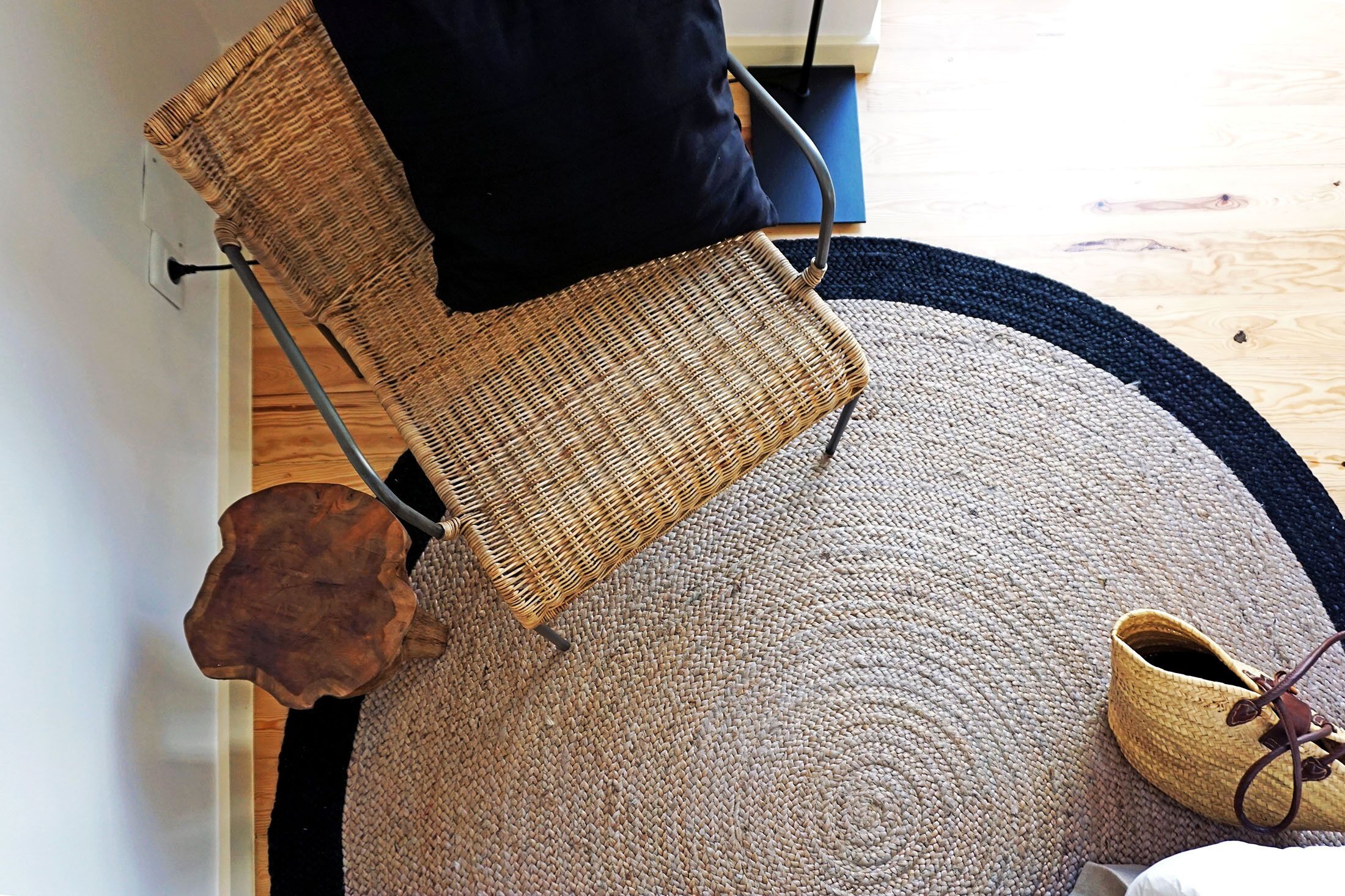 A room with a woven chair, a round rug, and a pair of shoes on the floor.