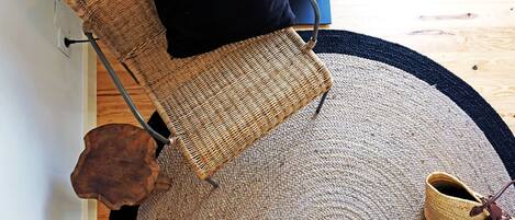 A room with a woven chair, a round rug, and a pair of shoes on the floor.