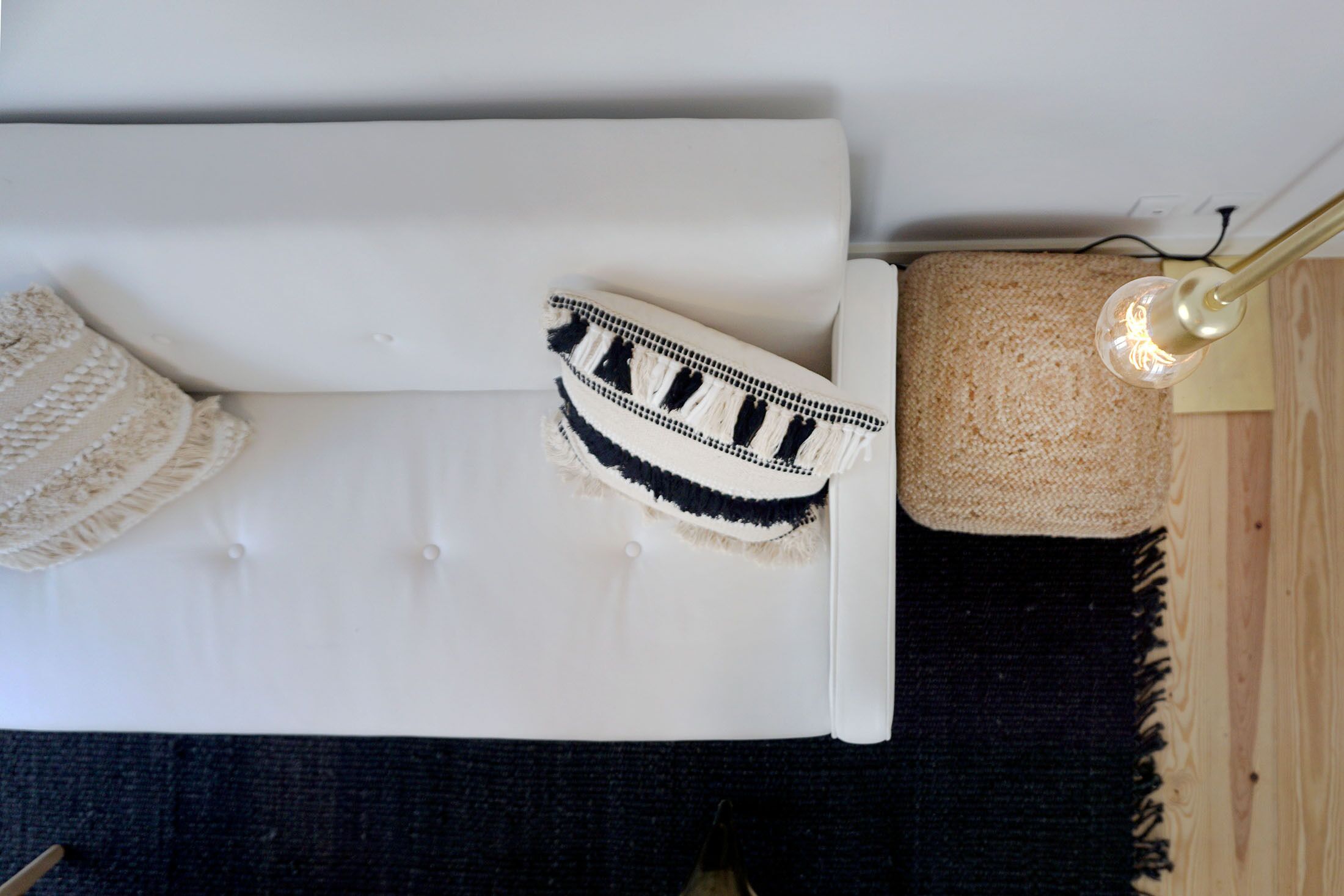 A white sofa with a decorative pillow and a small rug on the floor.