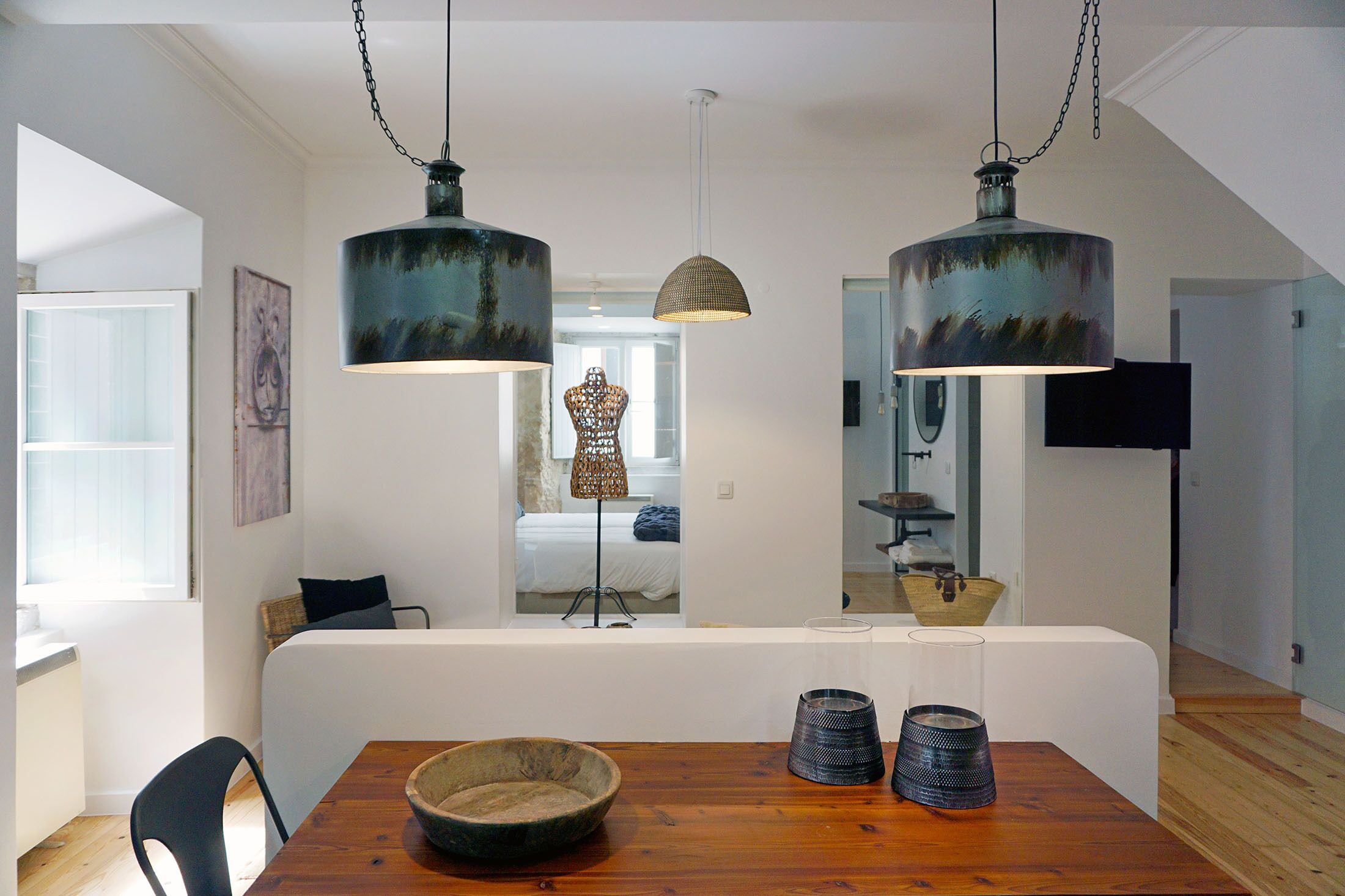 Een moderne eethoek met een houten tafel, twee hangende lampen en uitzicht op de aangrenzende slaapkamer.