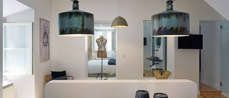Een moderne eethoek met een houten tafel, twee hangende lampen en uitzicht op de aangrenzende slaapkamer.