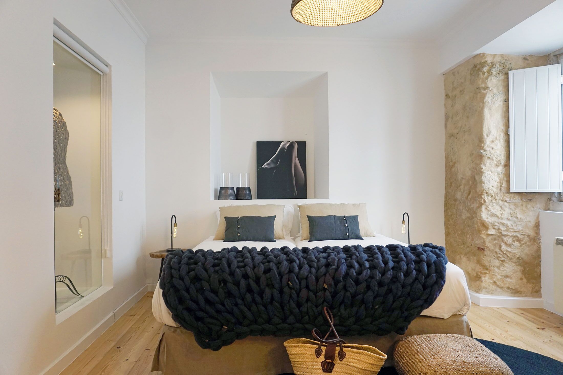 Een slaapkamer met een groot bed, een donkere deken, een schilderij aan de muur en een stenen muur.