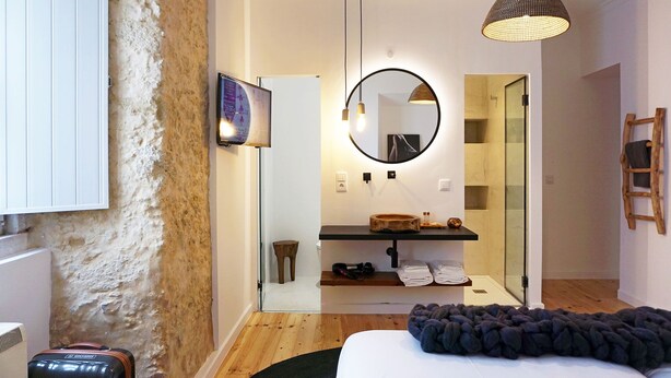 A modern bedroom with a large bed, a round mirror, a wooden shelf with toiletries, and a wooden floor.