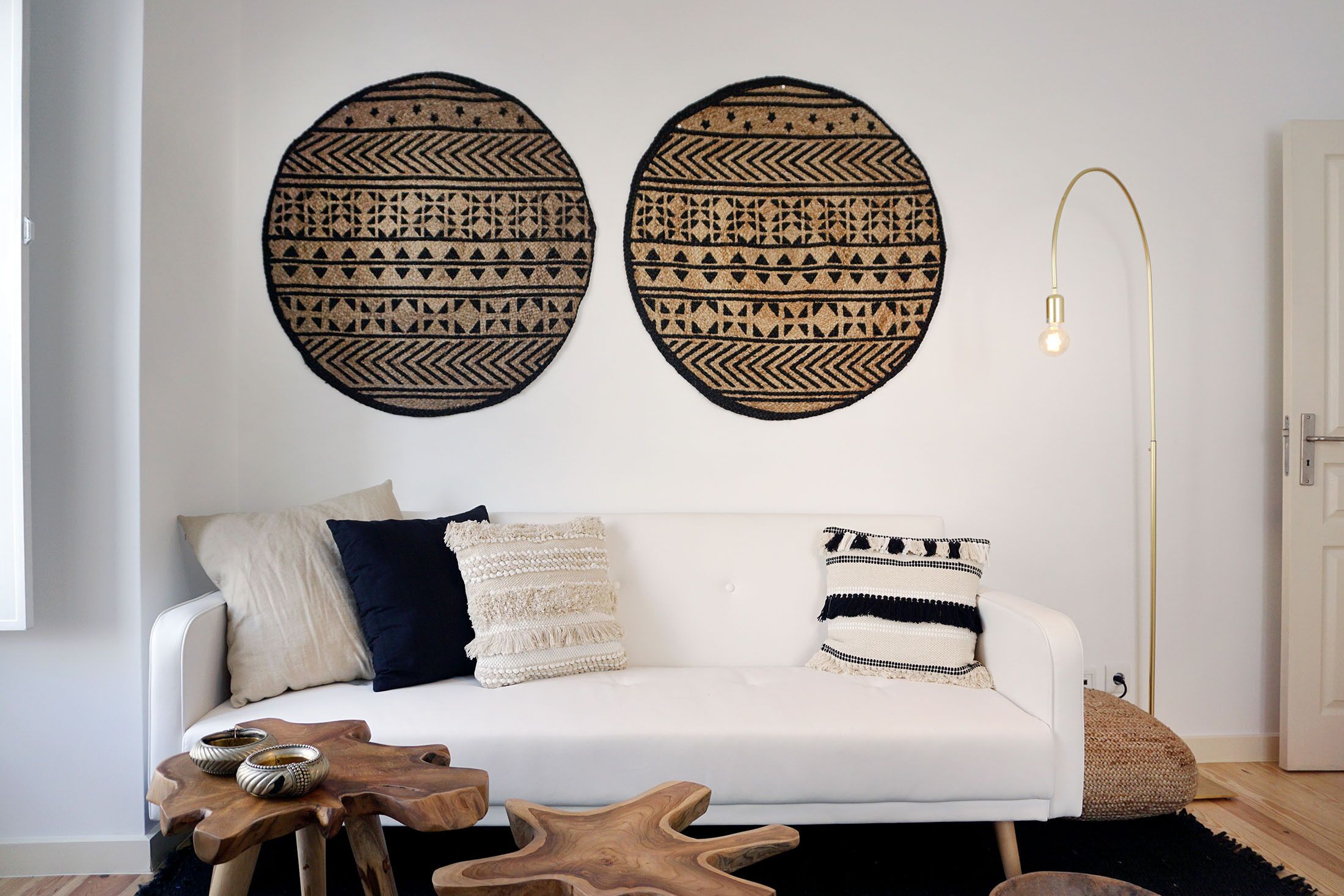 Un salon moderne avec un canapé blanc, deux éléments de décoration murale à motifs, une lampe sur pied et une table basse en bois.
