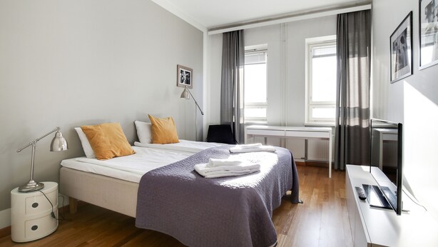 A modern hotel room with a neatly made bed, a desk with a computer, and a window with curtains. - Kotimaailma Aparthotel Kamppi - 2BR (Helsinki)