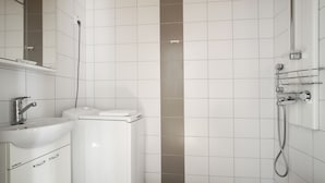 A modern bathroom with white tiles, a sink, a toilet, and a shower area. - Kotimaailma Aparthotel Kamppi - 2BR (Helsinki)