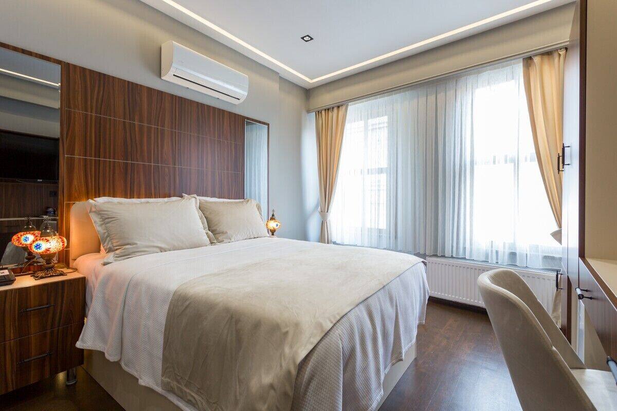 A modern hotel room with a large bed, a TV, an air conditioning unit, and a window with curtains.