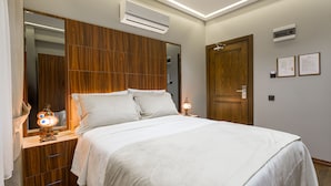 Una cama bien hecha con cabecera de madera, una lámpara de noche y un aire acondicionado instalado en la pared.