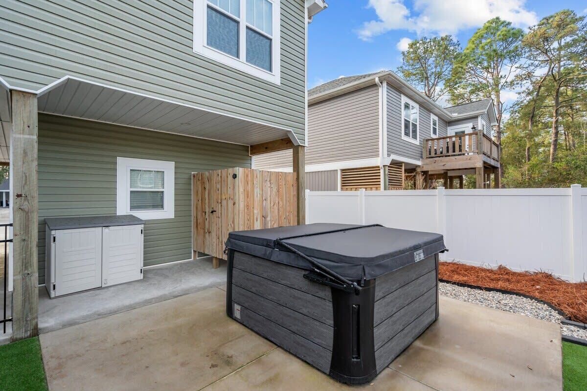 A backyard with a hot tub, a wooden deck, and a white fence.