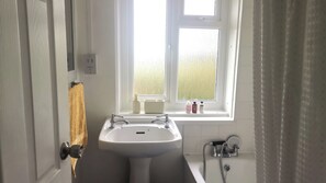Une salle de bain avec un lavabo blanc, une fenêtre donnant sur un beau paysage, une serviette accrochée à la porte et un espace douche.