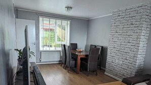 A room with a dining table, chairs, a TV, and a brick wall. - Seaview/downs National Park & Free Parking (Brighton)