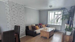 A living room with a brick wall, a sofa with cushions, a wooden coffee table, and a drum. - Seaview/downs National Park & Free Parking (Brighton)