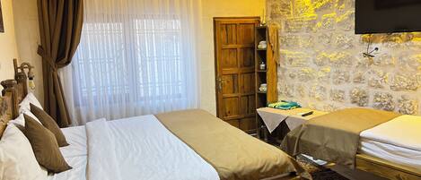 A hotel room with two beds, a wooden wardrobe, a small table, an air conditioning unit, and a television on the wall.