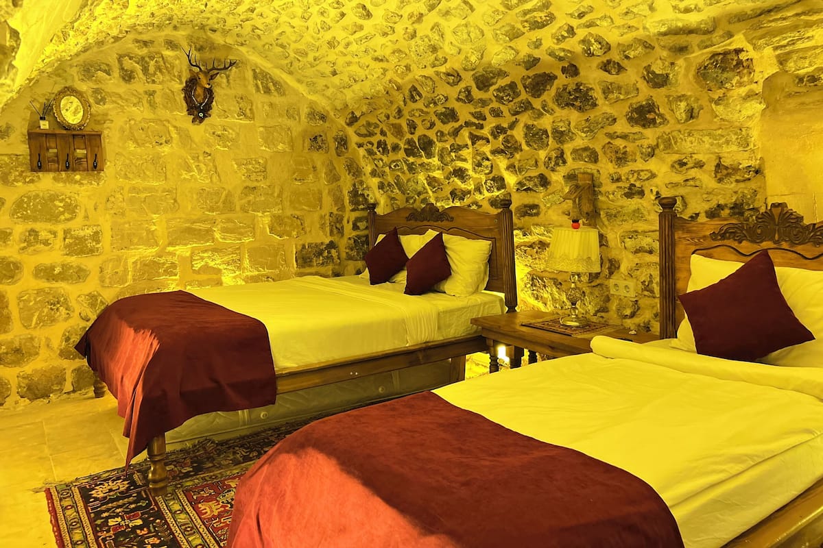 Quarto com paredes de pedra e duas camas com roupa de cama vermelha.
