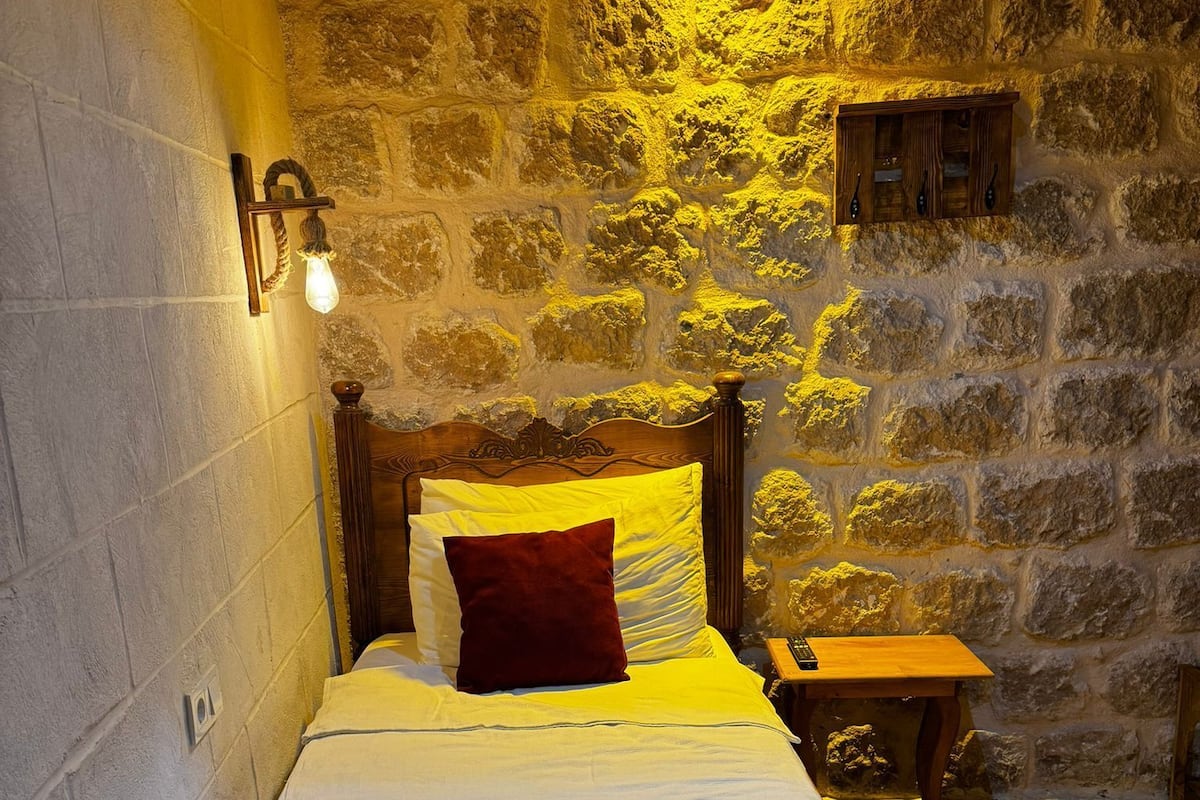 Uma cama de solteiro com cabeceira de madeira num quarto com paredes de pedra.