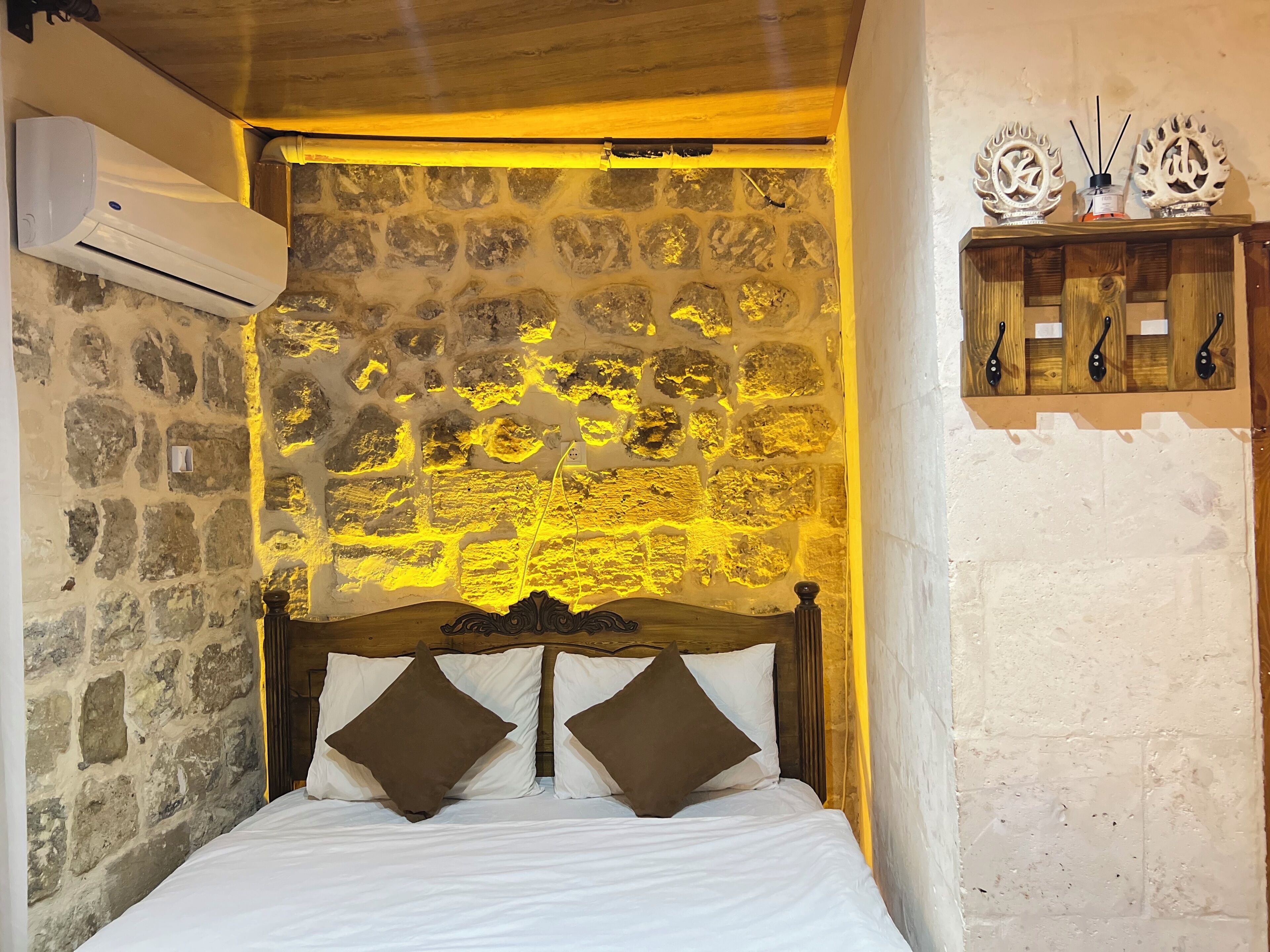 Un dormitorio con pared de piedra, cabecera de madera y cama con ropa de cama blanca y dos almohadas marrones.