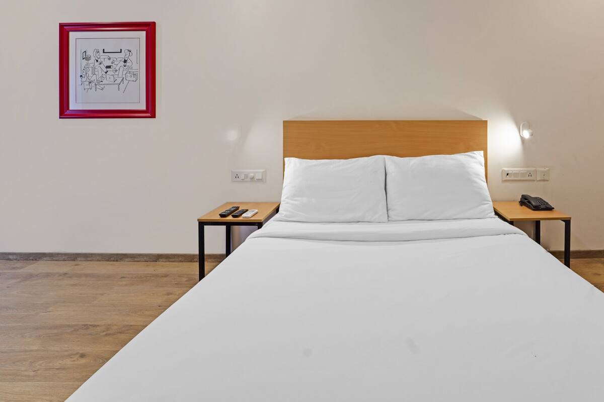 Una cama individual con ropa de cama blanca, cabecero de madera, mesitas de noche con teléfonos y un cuadro en la pared.