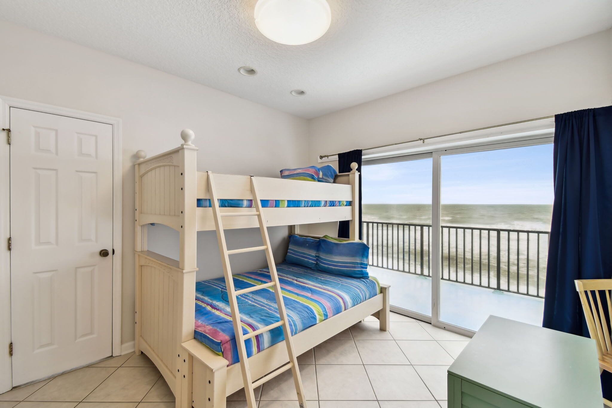 A room with a bunk bed, a small table, and a view of the beach through a balcony.