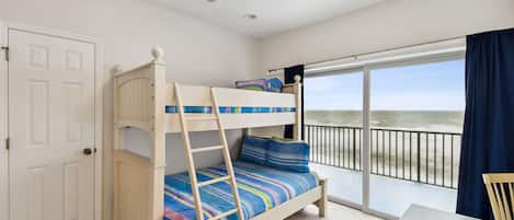 A room with a bunk bed, a small table, and a view of the beach through a balcony.