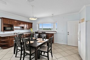 A kitchen with wooden cabinets, a dining table with chairs, a microwave, and a large window.
