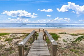 A wooden boardwalk leading to a beach with a clear view of the ocean and a sandy shore.
