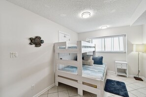 A bunk bed with a desk and lamp, a window, and a wall decoration.