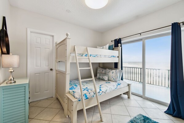 A bunk bed with a ladder, a door, a lamp, and a view of the outside.