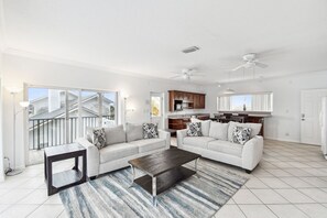 A spacious living room with a white sofa set, a coffee table, and a kitchen area in the background. - Dolphin View Oceanfront Home with Rooftop Deck (Ponte Vedra Beach)