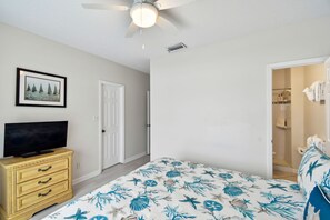 A bedroom with a bed, a television on a dresser, a ceiling fan, and a door leading to a bathroom. - Dolphin View Oceanfront Home with Rooftop Deck (Ponte Vedra Beach)