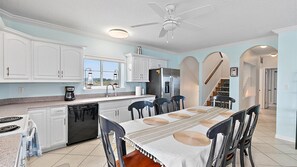 A modern kitchen with white cabinets, a dishwasher, a refrigerator, and a dining area with a table and chairs.
