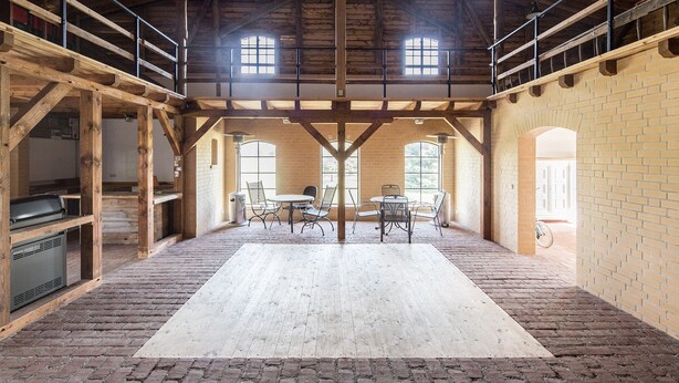 A spacious room with a high wooden ceiling, brick walls, and a large central table with chairs.