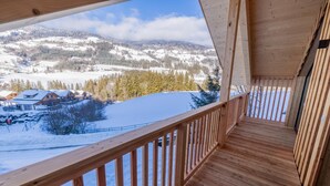 A wooden deck with a view of snow-covered hills and houses.