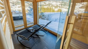 A sauna room with a glass door, wooden interior, and a view of a snowy landscape.