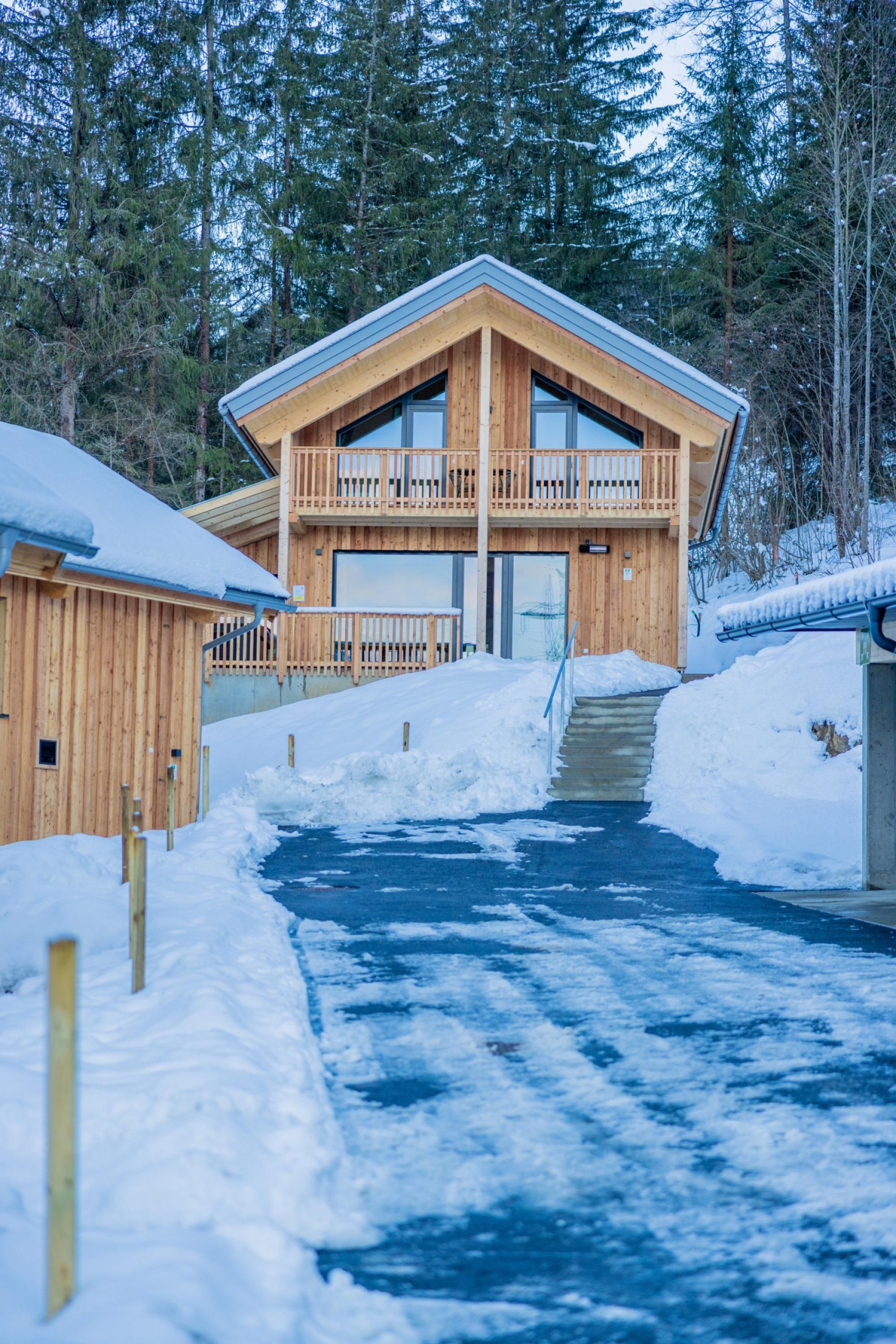 A wooden lodge with a balcony, a covered entrance, and a snow-covered path leading to the main building.