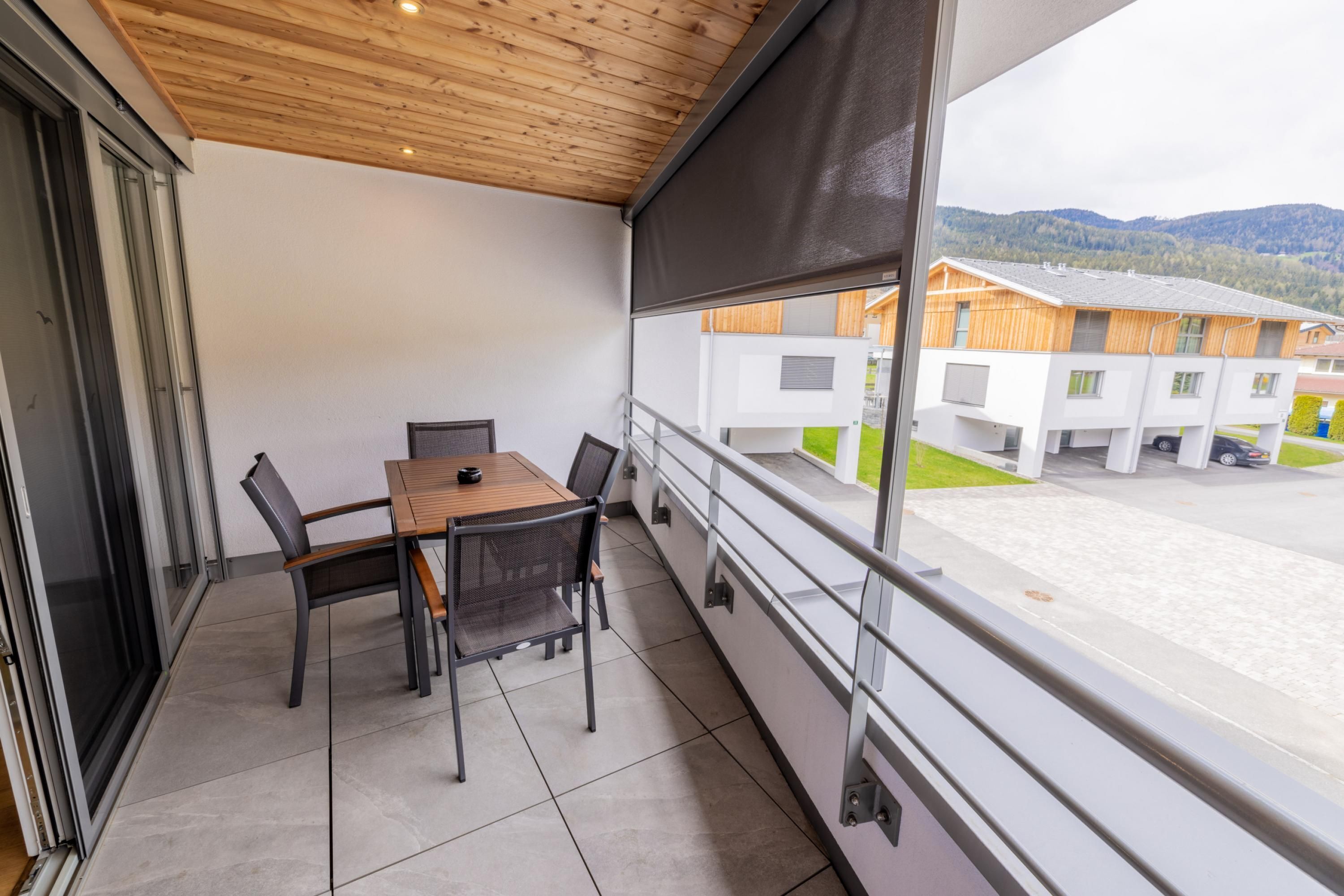 A balcony with a table and chairs, a view of buildings and mountains, and a wooden ceiling.
