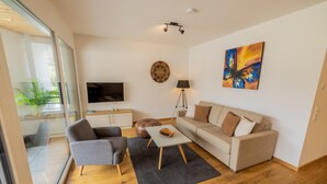 Un soggiorno moderno con un divano, poltrone, un tavolino, una televisione e un quadro appeso al muro.