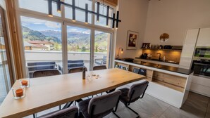 A modern kitchen with a large wooden table, built-in cabinets, and a view of the mountains through large windows. - 070 Phkb9 in St Georgen am Kreischberg (Sankt Georgen am Kreischberg)