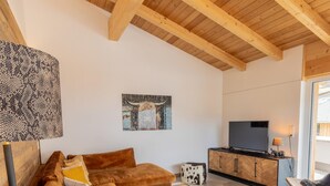 A modern living room with a wooden ceiling, a sectional sofa, a coffee table, a television on a cabinet, and a large window. - 070 Phkb9 in St Georgen am Kreischberg (Sankt Georgen am Kreischberg)
