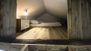 Una piccola camera da letto in stile mansarda, con soffitto e pareti in legno, un letto singolo, un comodino con una lampada e un pavimento in legno.