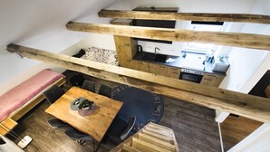 Una stanza in stile loft con soffitto in legno, un'area pranzo con tavolo e sedie, un angolo cottura e un letto con copripiumino decorato.