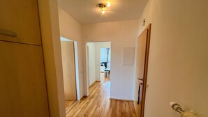 A hallway with wooden flooring leading to a room with a door and a light fixture on the ceiling.