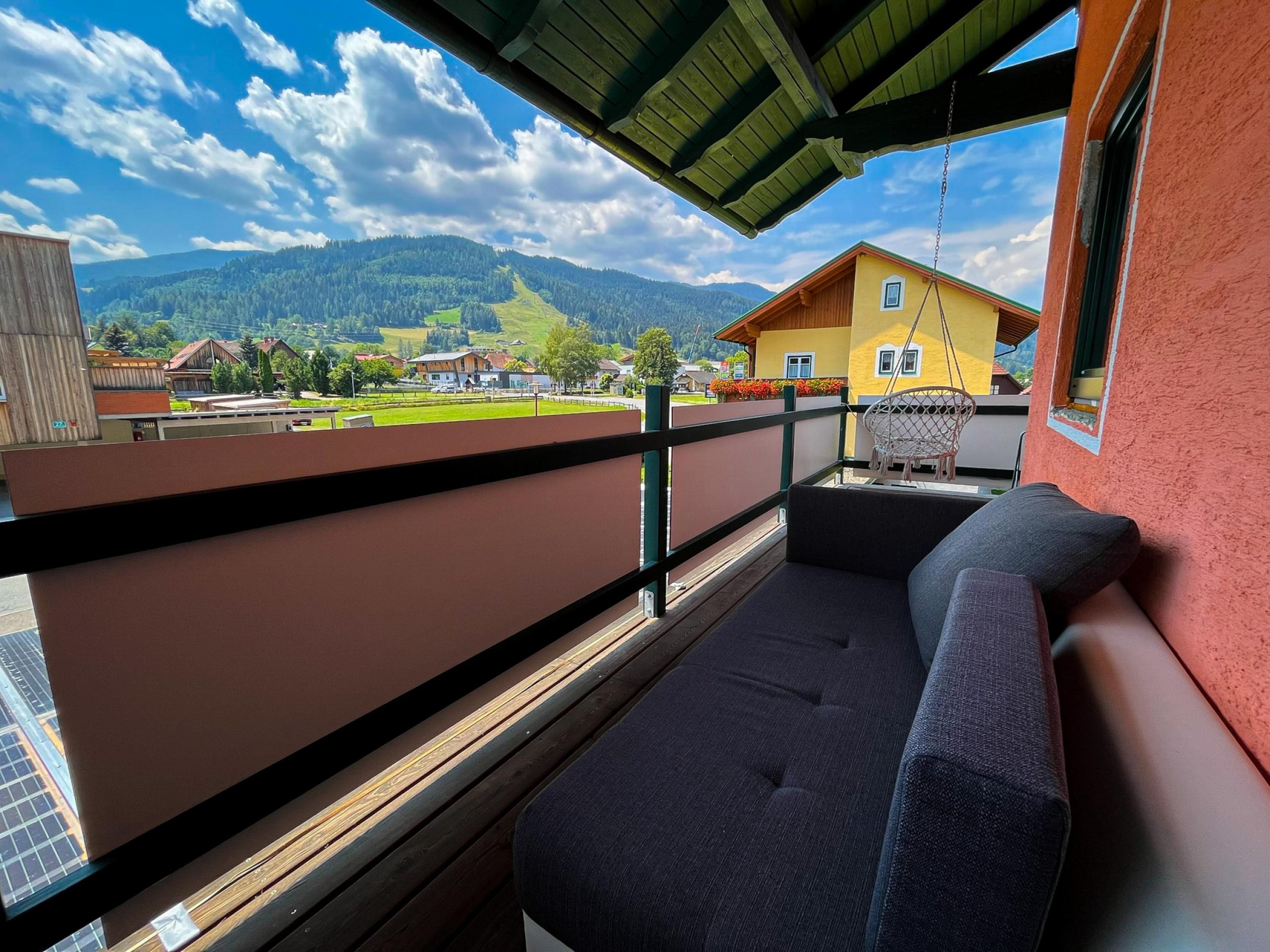 A balcony with a view of a mountain landscape, a yellow building, and a red wall.